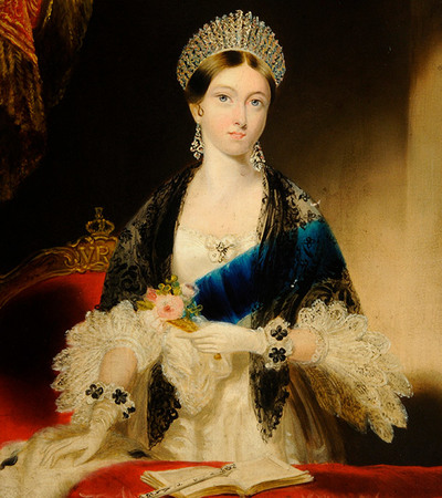 Portrait of a woman staring straight at the artist. She is wearing a crown with jewels and a black shawl over a blue dress. She is holding a flower in one hand and the other rests on the chair in front of her. There is an open book in front of her.